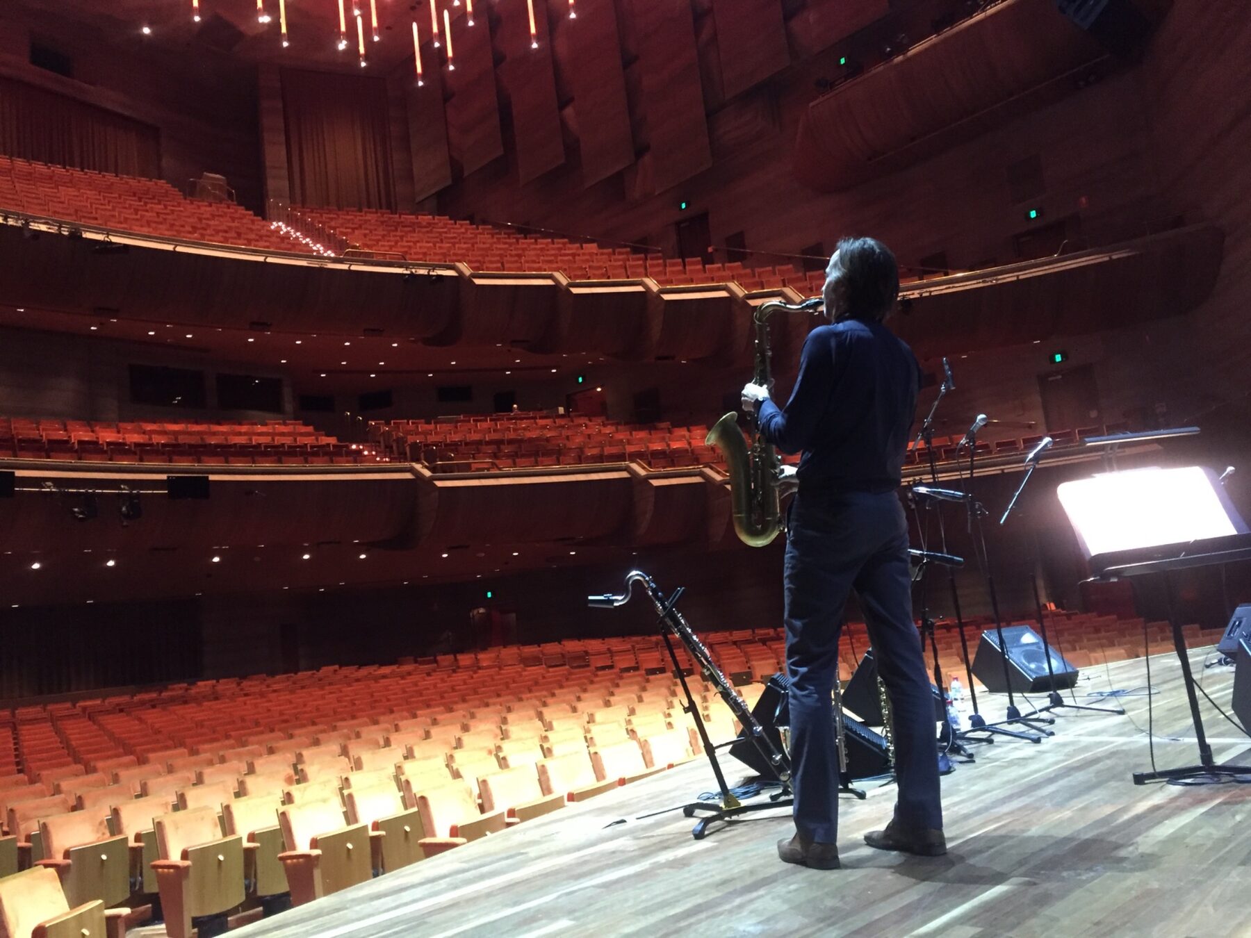 A saxophonist soundchecking on stage in an empty theatre